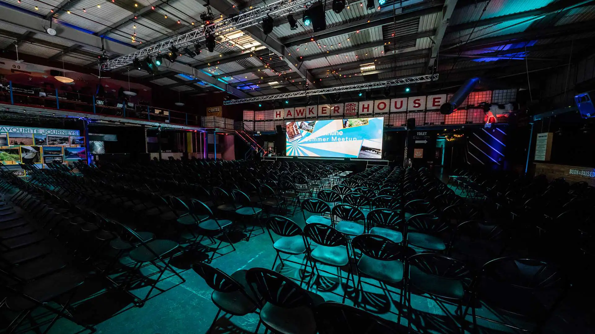 A large venue space set out with chairs facing a stage, with a huge screen
