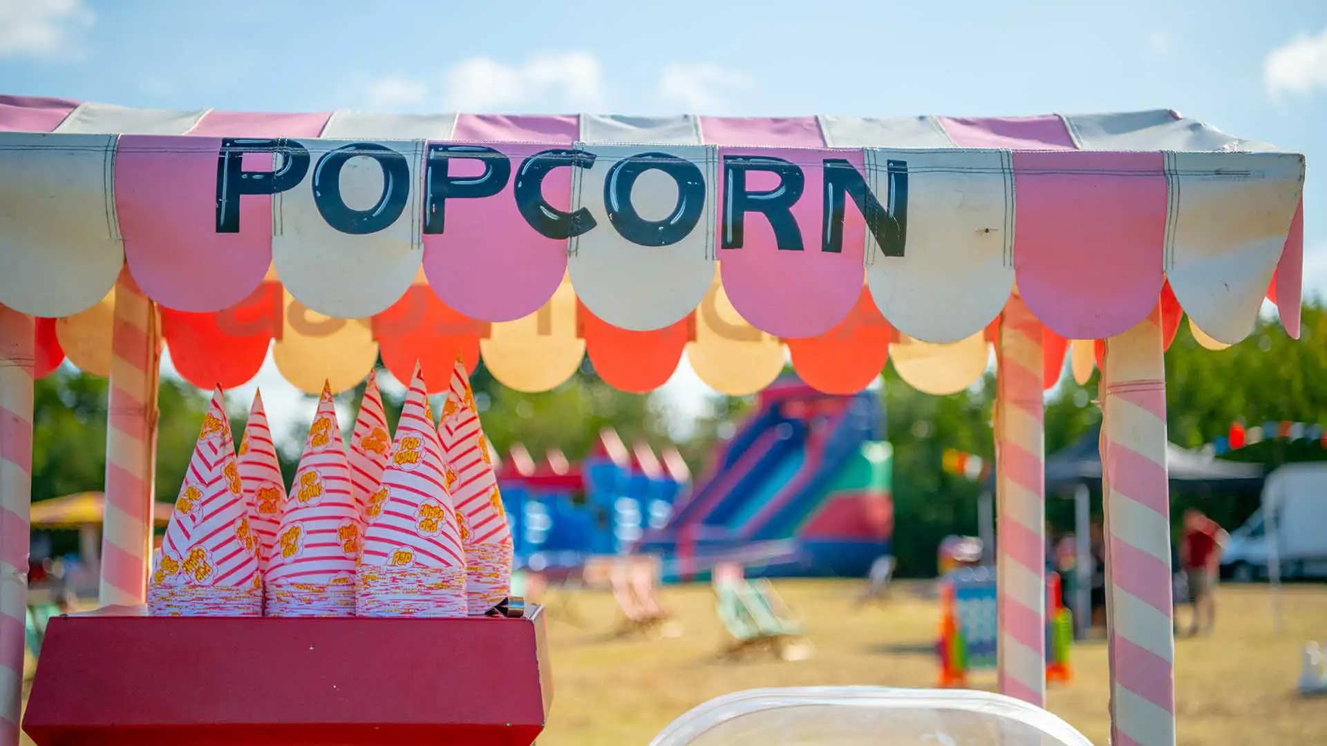 6 amazing and creative corporate event ideas | MGN Events A close up image of a popcorn machine with festiva games and tents in the background. corporate event ideas