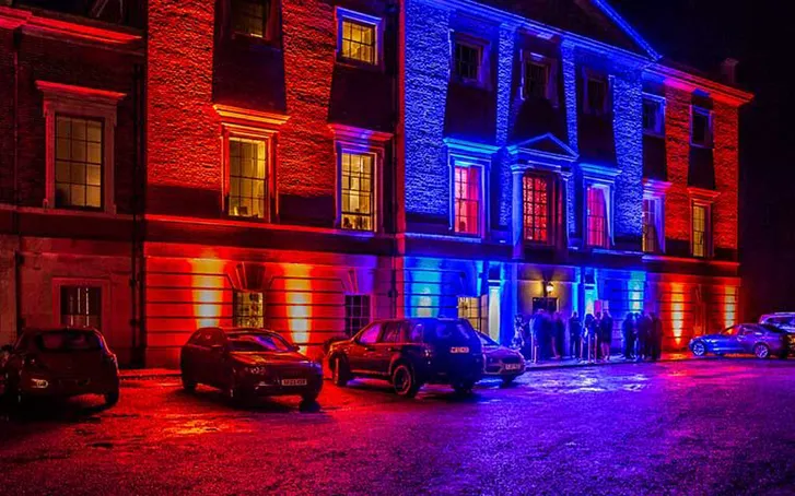 A beautiful building up-lit from the outside, with cars parked along its front