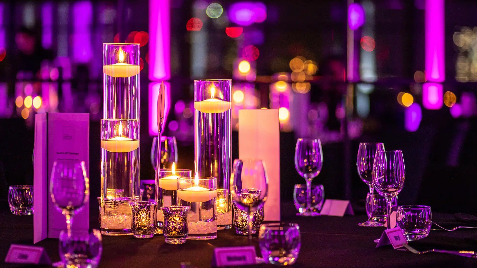 Many mixed sized candles with purple uplighters